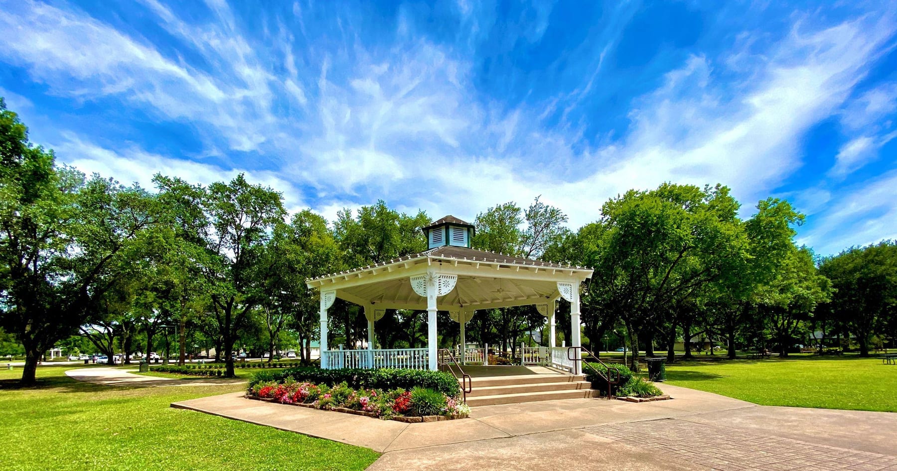 A white gazebo surrounded by mature oak trees in a Friendswood park