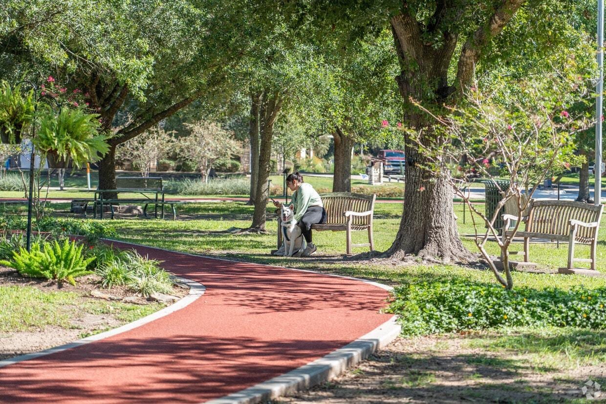 A resident walking her dog along a shaded park trail in Friendswood